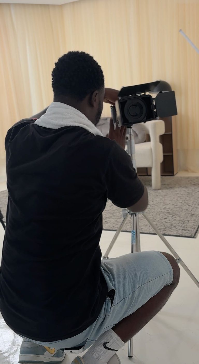 A CROP House photographer seated on set, shooting with a camera under softbox lighting on location in Lagos.